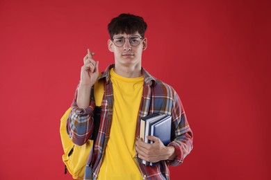Photo of Worried student with books crossing fingers for good exam result on red background