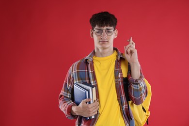 Photo of Worried student with books crossing fingers for good exam result on red background