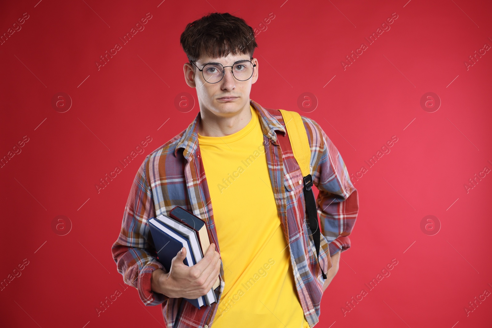 Student with books worried about his exam result on red background Photo of Student with books worried about his exam result on red background