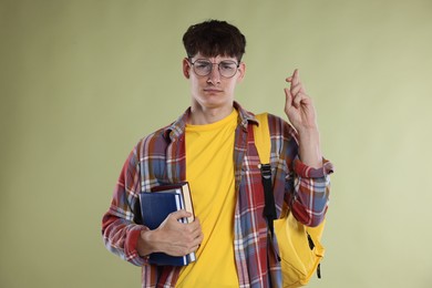 Photo of Worried student crossing fingers for good exam result on light olive background
