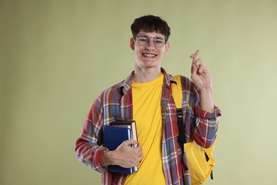 Photo of Happy student crossing fingers for good exam result on light olive background