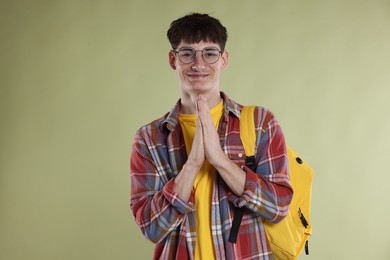Photo of Student with clasped hands praying for good exam result on light olive background