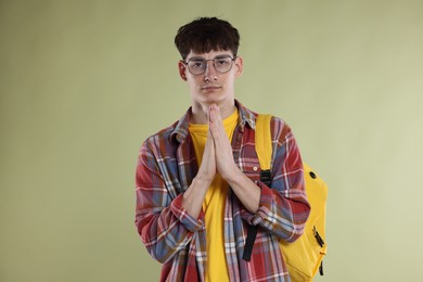 Photo of Student with clasped hands praying for good exam result on light olive background