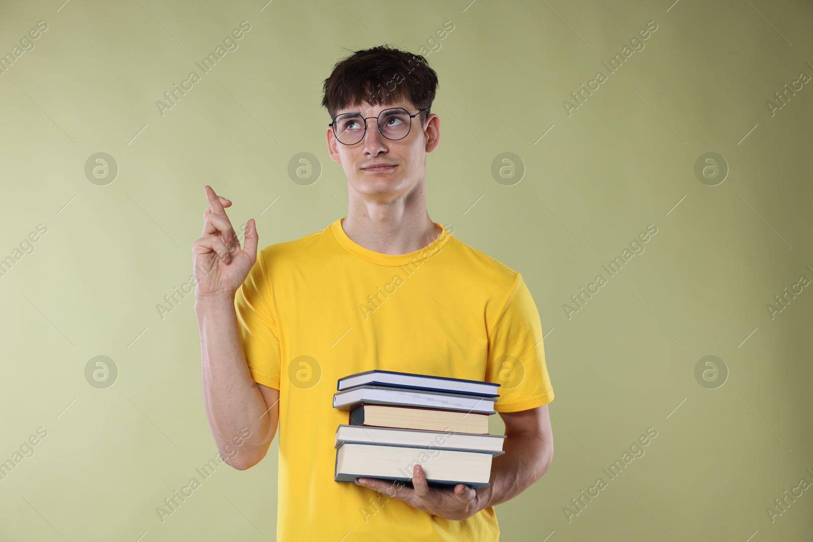 Worried student crossing fingers for good exam result on light olive background Photo of Worried student crossing fingers for good exam result on light olive background