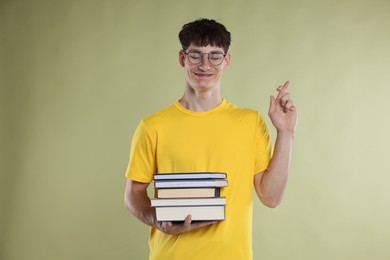 Photo of Happy student crossing fingers for good exam result on light olive background