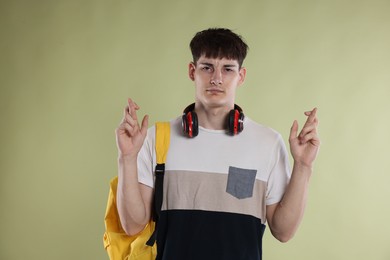Photo of Worried student crossing fingers for good exam result on light olive background
