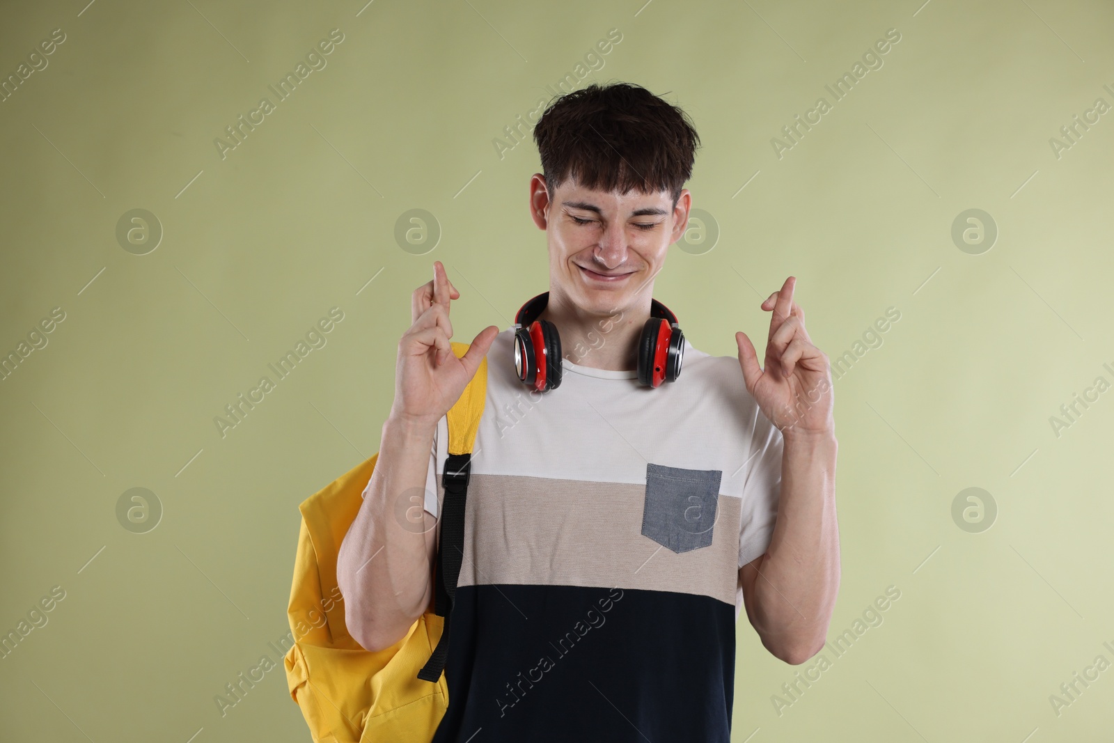 Happy student crossing fingers for good exam result on light olive background Photo of Happy student crossing fingers for good exam result on light olive background