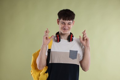Photo of Happy student crossing fingers for good exam result on light olive background