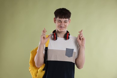 Photo of Happy student crossing fingers for good exam result on light olive background