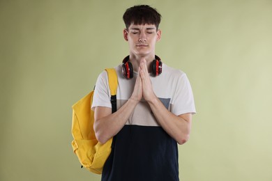 Photo of Student with clasped hands praying for good exam result on light olive background