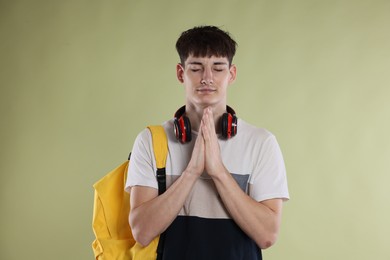Photo of Student with clasped hands praying for good exam result on light olive background