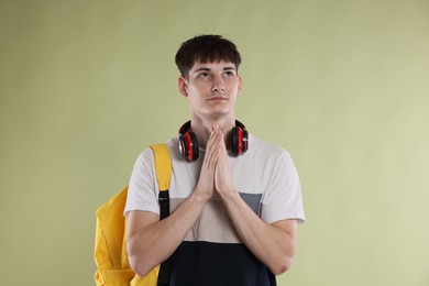 Photo of Student with clasped hands praying for good exam result on light olive background