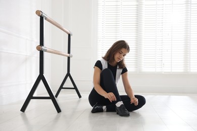 Photo of Teenage girl tying shoelace of tap shoe indoors