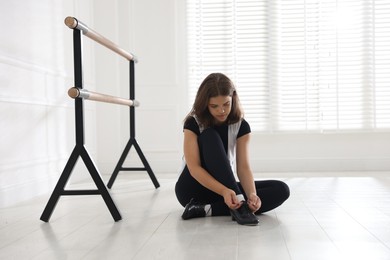 Photo of Teenage girl tying shoelace of tap shoe indoors