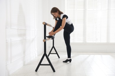 Photo of Teenage girl tying shoelace of tap shoe near barre indoors