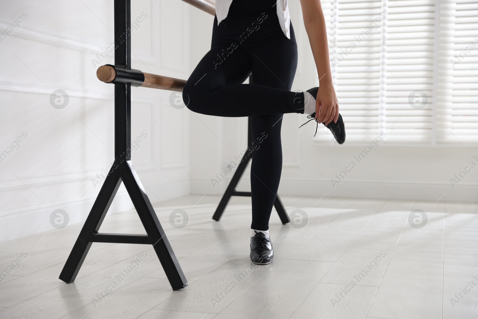 Photo of Teenage girl in tap shoes stretching at barre indoors, closeup