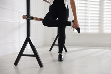 Photo of Teenage girl in tap shoes stretching at barre indoors, closeup