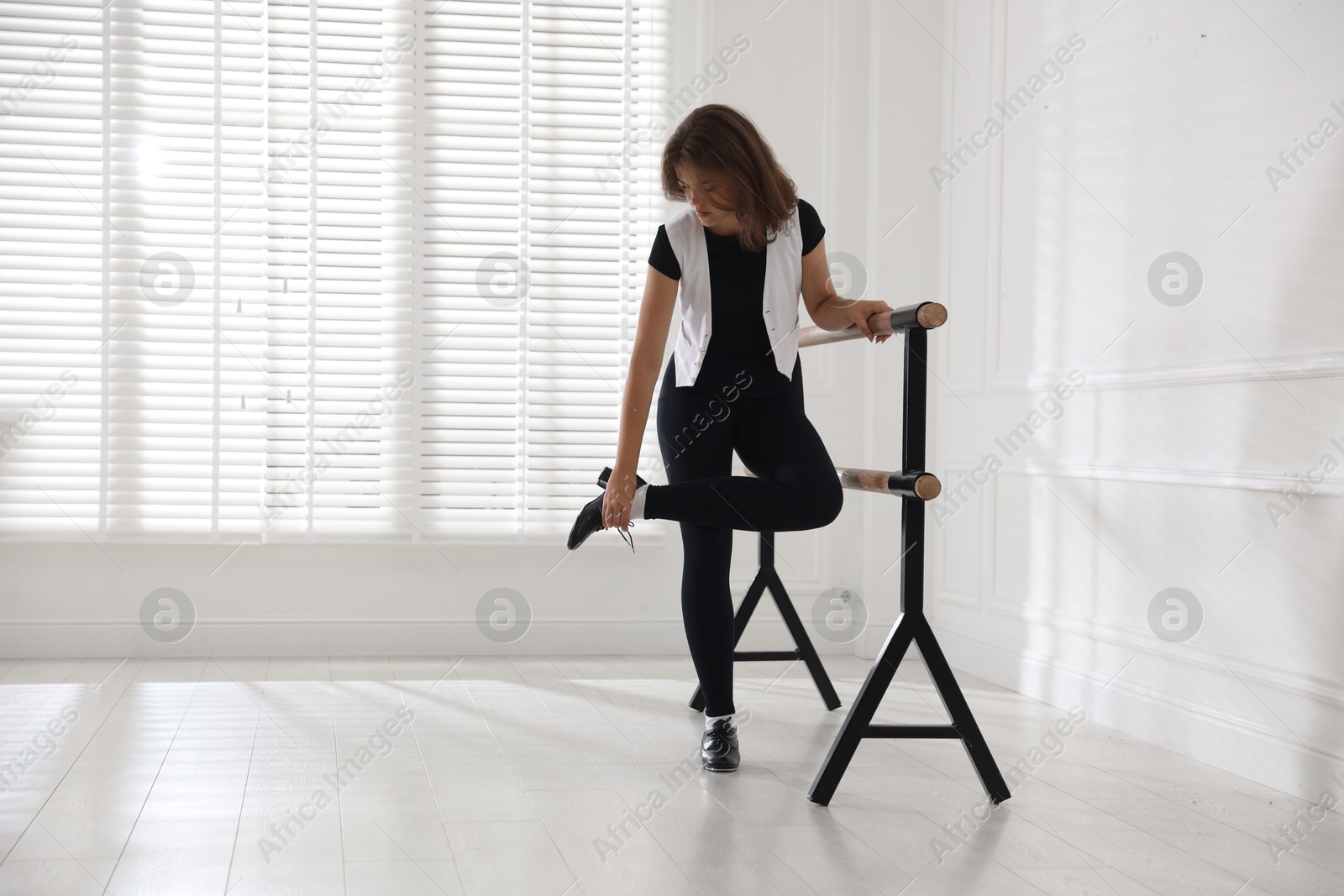 Teenage girl in tap shoes stretching at barre indoors Photo of Teenage girl in tap shoes stretching at barre indoors