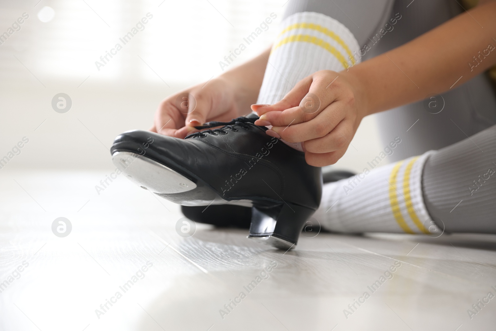 Photo of Teenage girl tying shoelace of tap shoe indoors, closeup