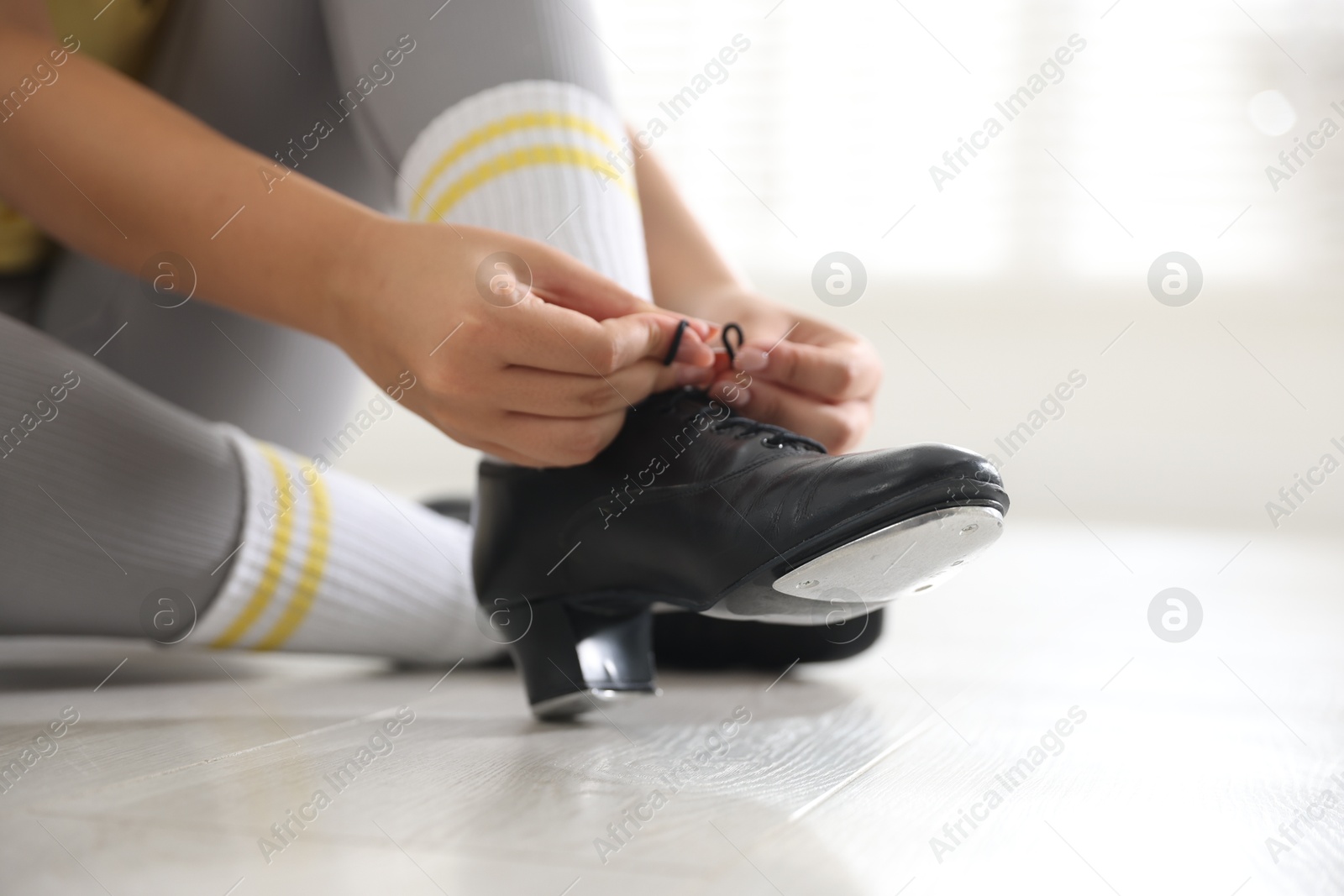 Photo of Teenage girl tying shoelace of tap shoe indoors, closeup
