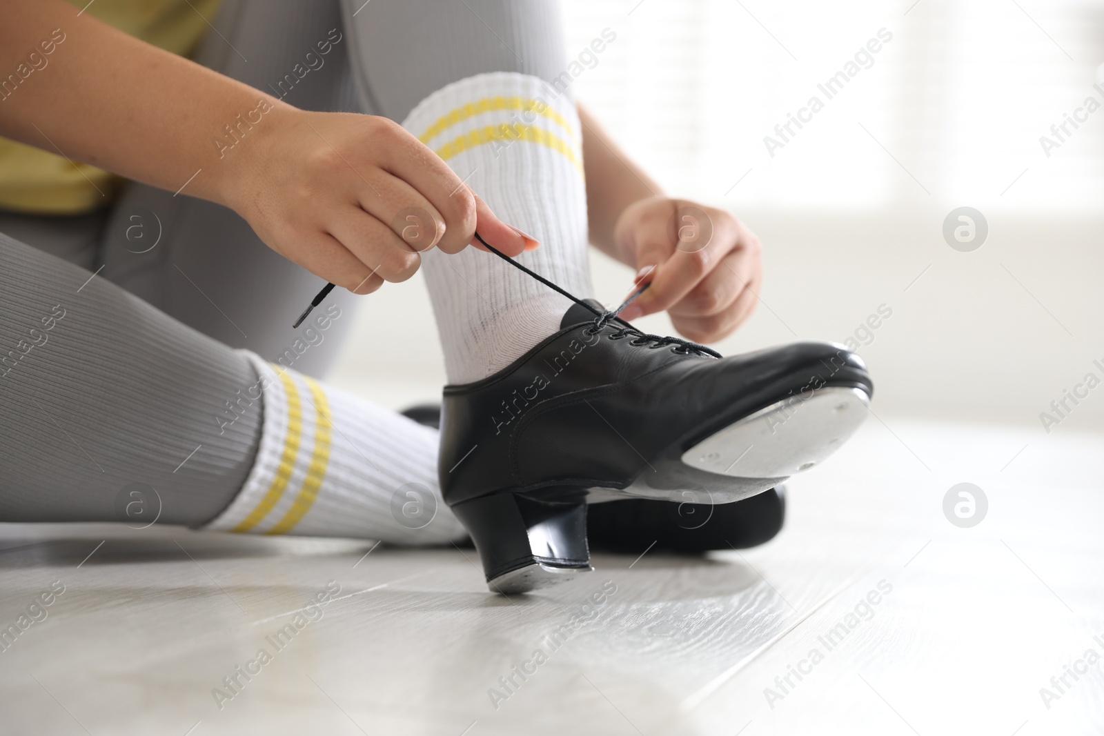 Photo of Teenage girl tying shoelace of tap shoe indoors, closeup