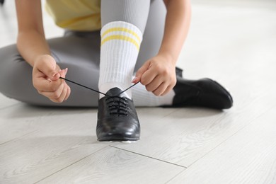 Photo of Teenage girl tying shoelace of tap shoe indoors, closeup