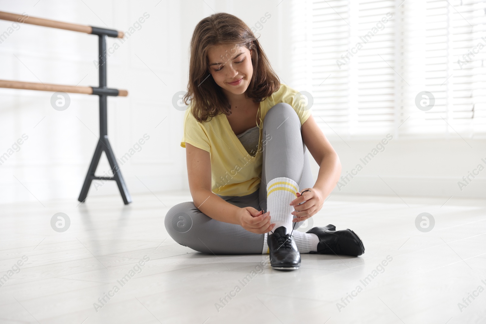 Teenage girl tying shoelace of tap shoe indoors Photo of Teenage girl tying shoelace of tap shoe indoors