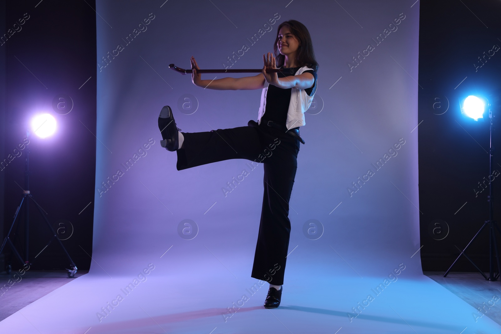 Teenage girl in tap shoes with cane dancing on color background Photo of Teenage girl in tap shoes with cane dancing on color background