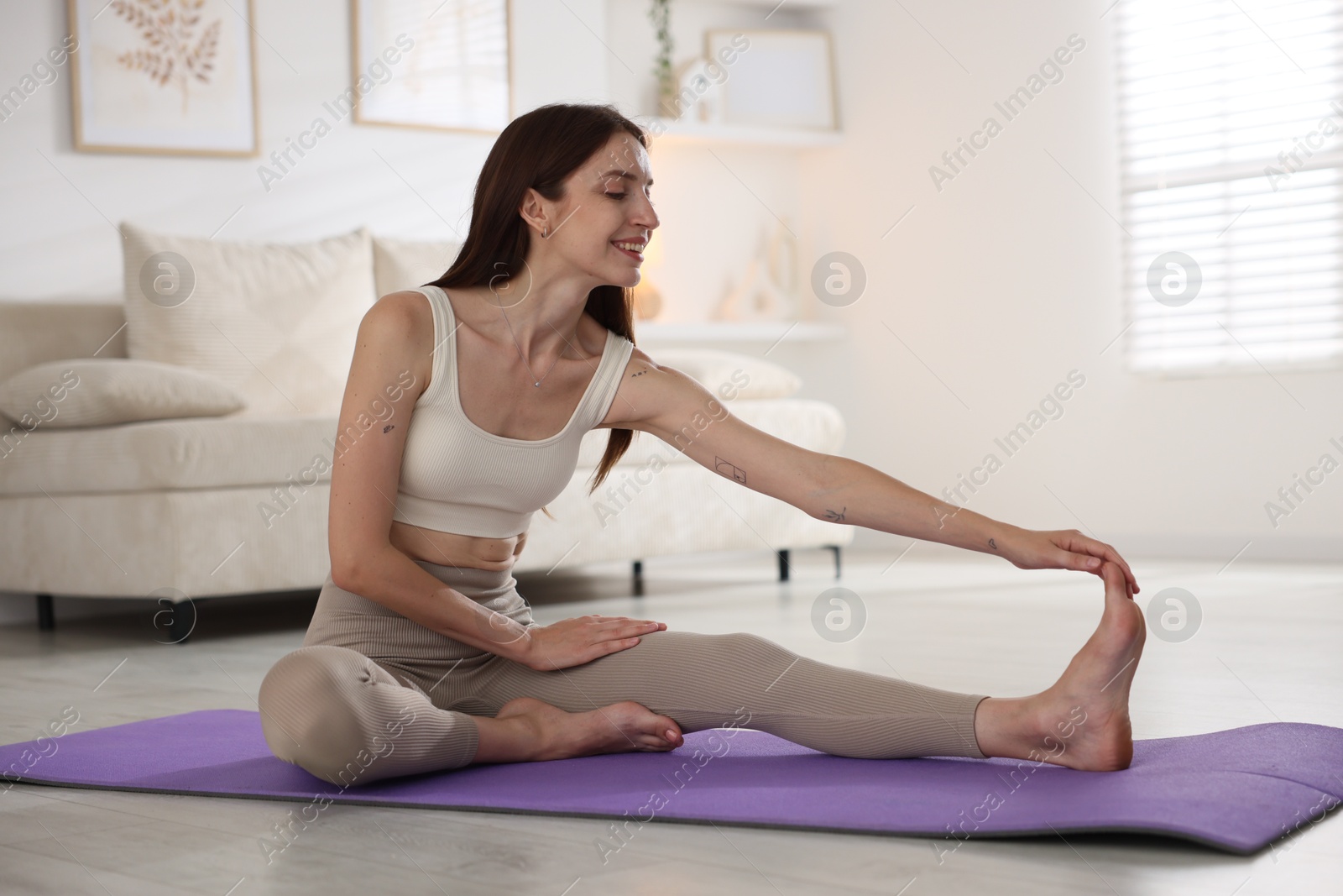 Smiling woman in sportswear stretching on mat at home Photo of Smiling woman in sportswear stretching on mat at home