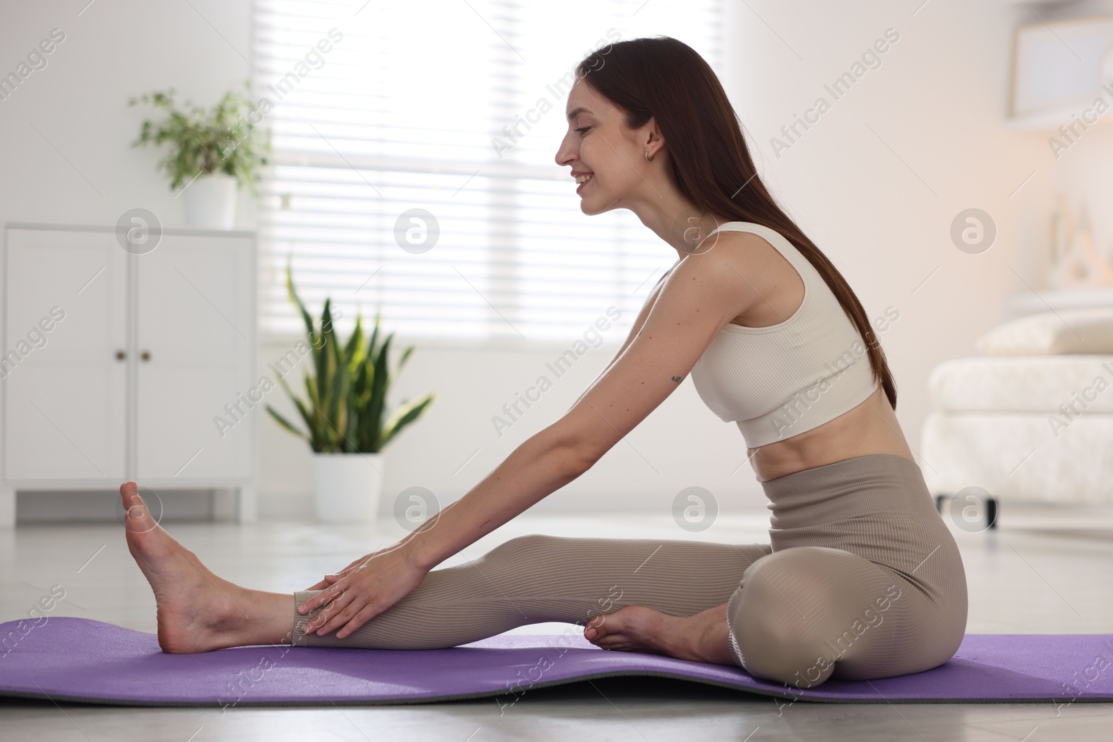 Smiling woman in sportswear stretching on mat at home Photo of Smiling woman in sportswear stretching on mat at home