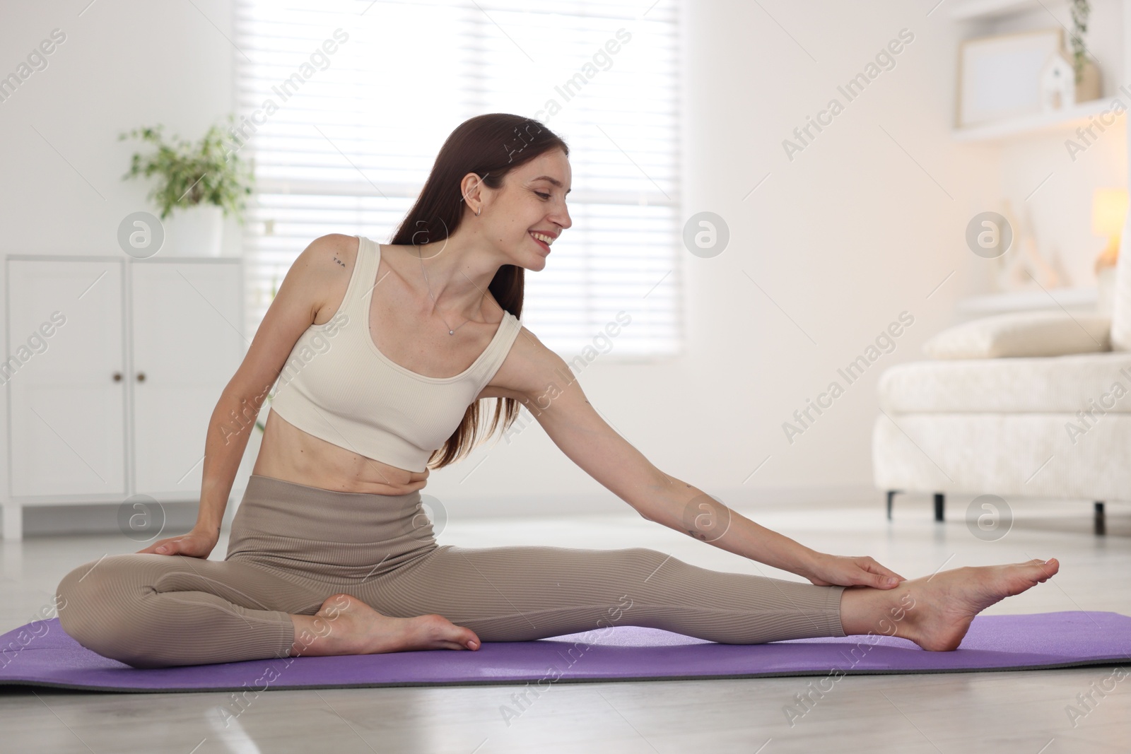 Smiling woman in sportswear stretching on mat at home Photo of Smiling woman in sportswear stretching on mat at home