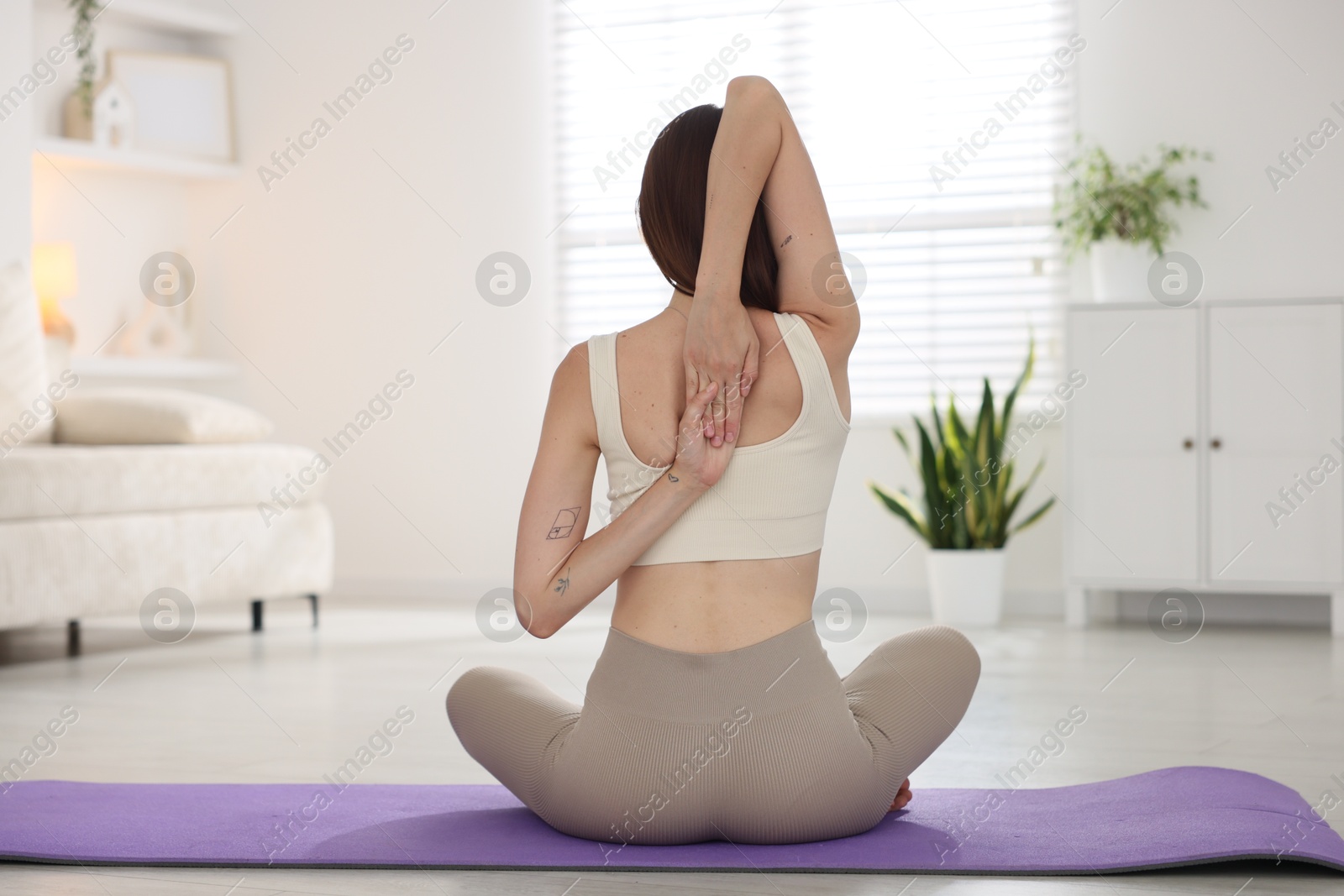 Woman in sportswear stretching on mat at home, back view Photo of Woman in sportswear stretching on mat at home, back view
