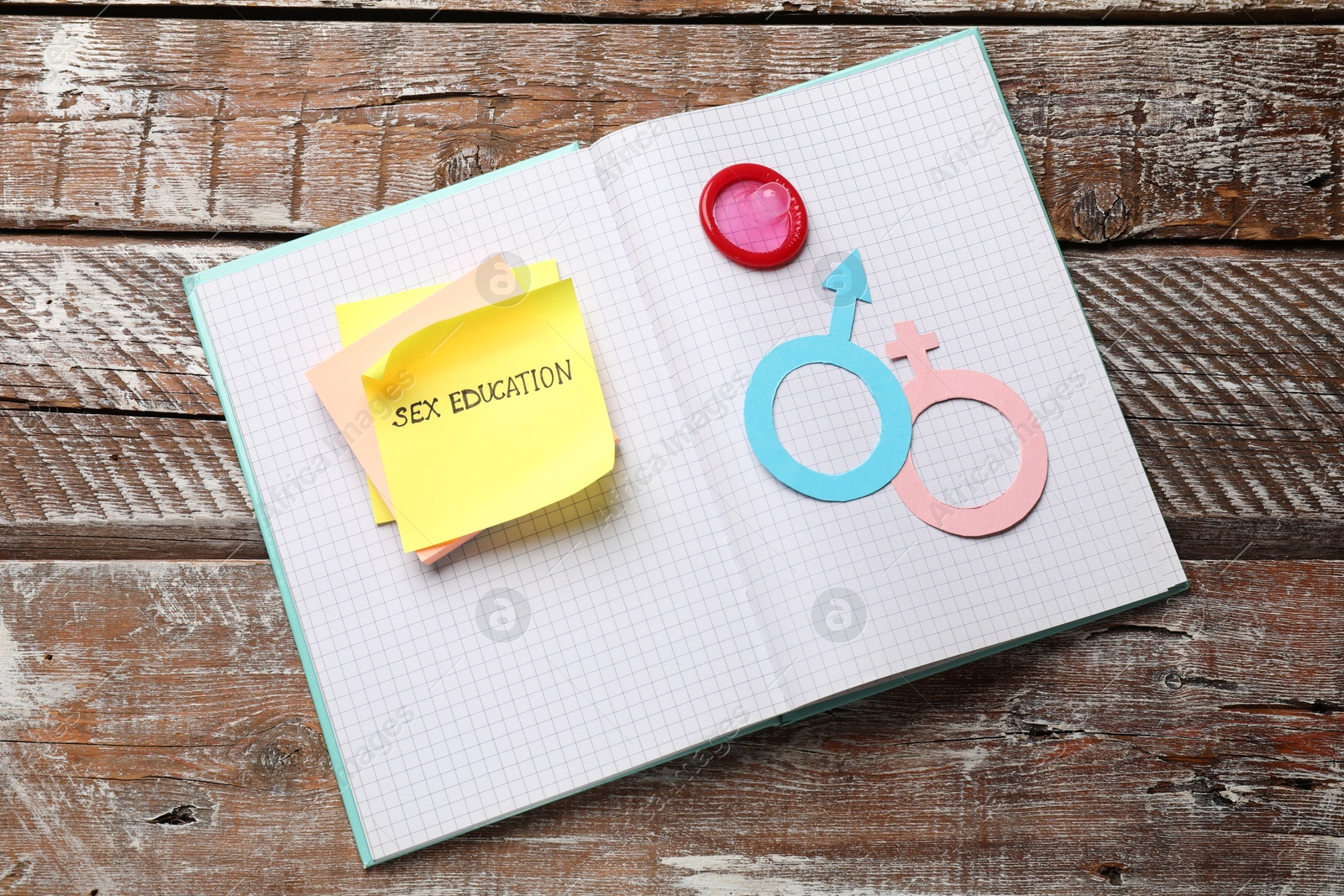 Photo of Sticky notes with phrase Sex Education, paper female and male gender symbols in notebook on wooden table, top view