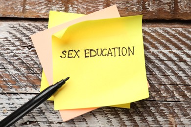 Photo of Sticky notes with phrase Sex Education and felt tip pen on wooden background, top view