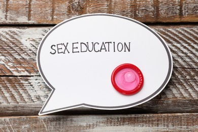 Photo of Speech bubble with phrase Sex Education and condom on wooden background, top view