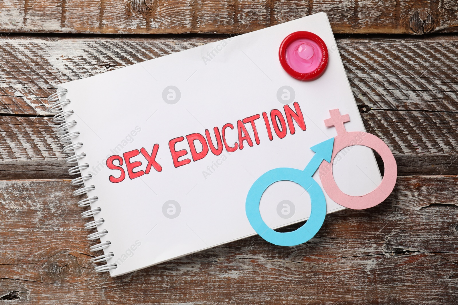 Photo of Notebook with phrase Sex Education, paper female and male gender symbols on wooden table, top view