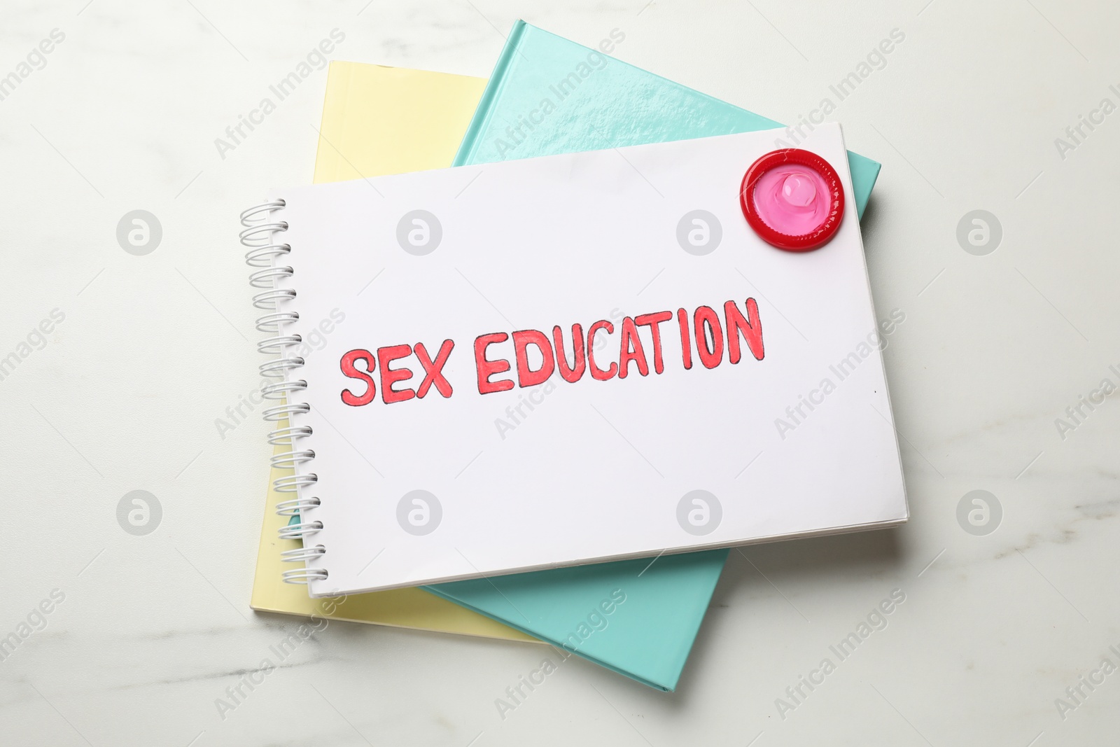 Photo of Notebooks with phrase Sex Education and condom on white background, top view