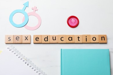 Photo of Phrase Sex Education made with wooden letters, condom, paper female and male gender symbols, notebooks on white background, flat lay