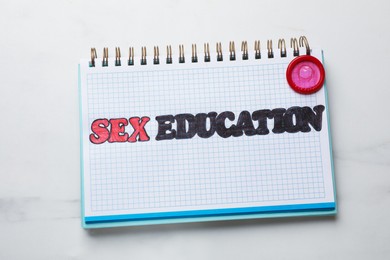 Photo of Phrase Sex Education written in notebook and condom on white background, top view