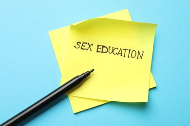Photo of Sticky notes with phrase Sex Education and felt tip pen on light blue background, top view