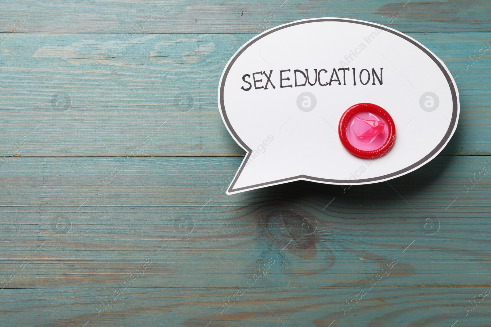Photo of Speech bubble with phrase Sex Education and condom on blue wooden background, top view