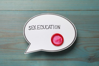 Photo of Speech bubble with phrase Sex Education and condom on blue wooden background, top view