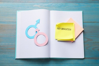 Photo of Sticky notes with phrase Sex Education, paper female and male gender symbols in notebook on blue wooden table, top view
