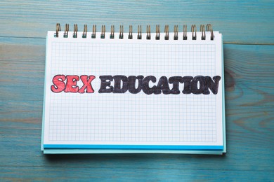Photo of Phrase Sex Education written in notebook on blue wooden table, top view