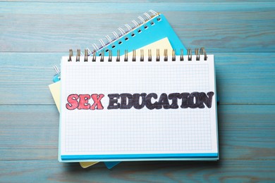 Photo of Notebooks with phrase Sex Education on blue wooden background, top view