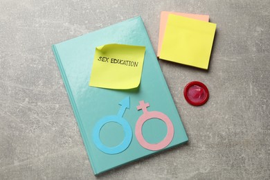 Photo of Sticky note with phrase Sex Education, paper female and male gender symbols, notebook, condom on grey table, flat lay
