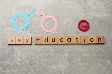 Photo of Phrase Sex Education made of wooden letters, condom, paper female and male gender symbols on grey table, flat lay
