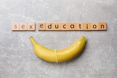 Photo of Phrase Sex Education made of wooden letters and banana with condom on grey table, flat lay