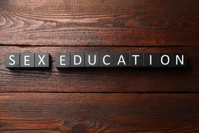 Photo of Phrase Sex Education made with cubes on wooden table, top view
