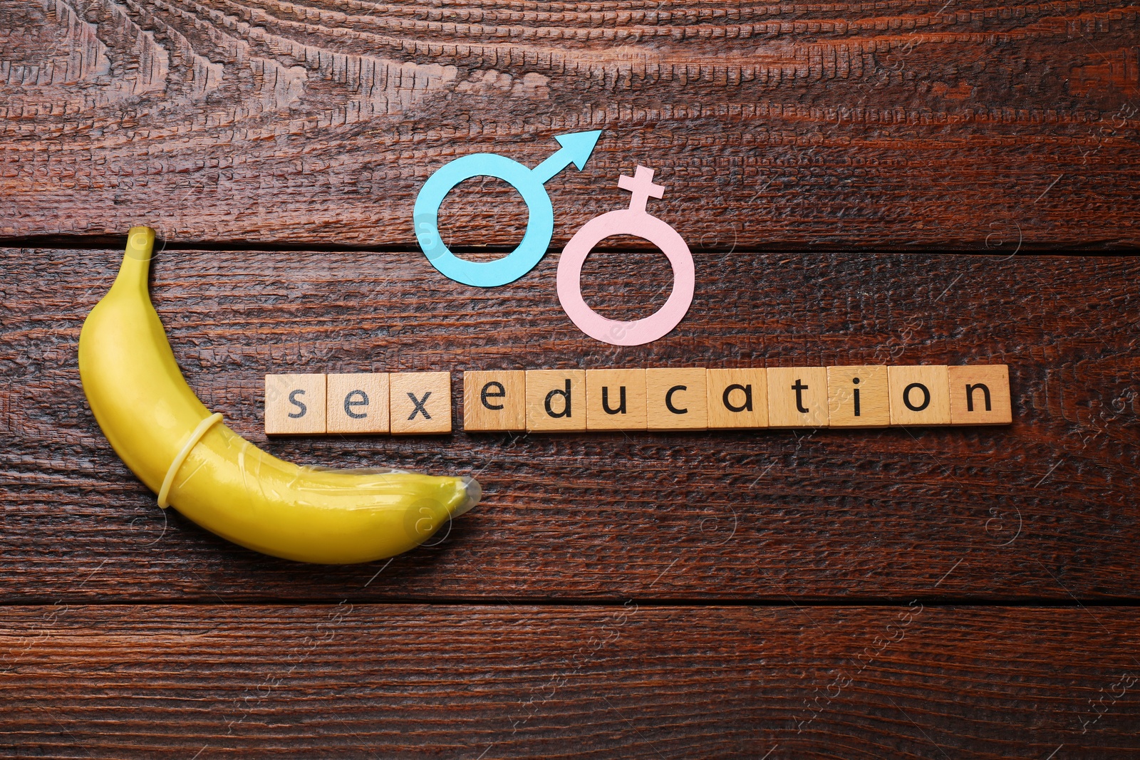 Photo of Phrase Sex Education made of wooden letters, banana with condom, paper female and male gender symbols on table, flat lay